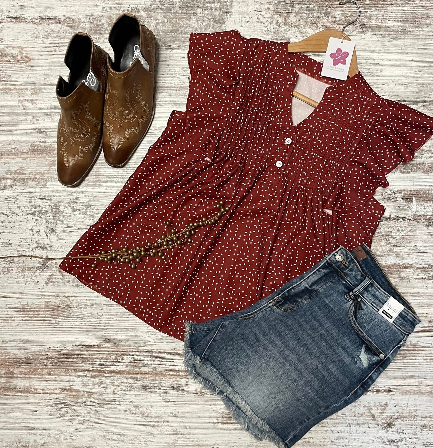 Red polka dot blouse with denim shorts and brown boots on a wooden surface