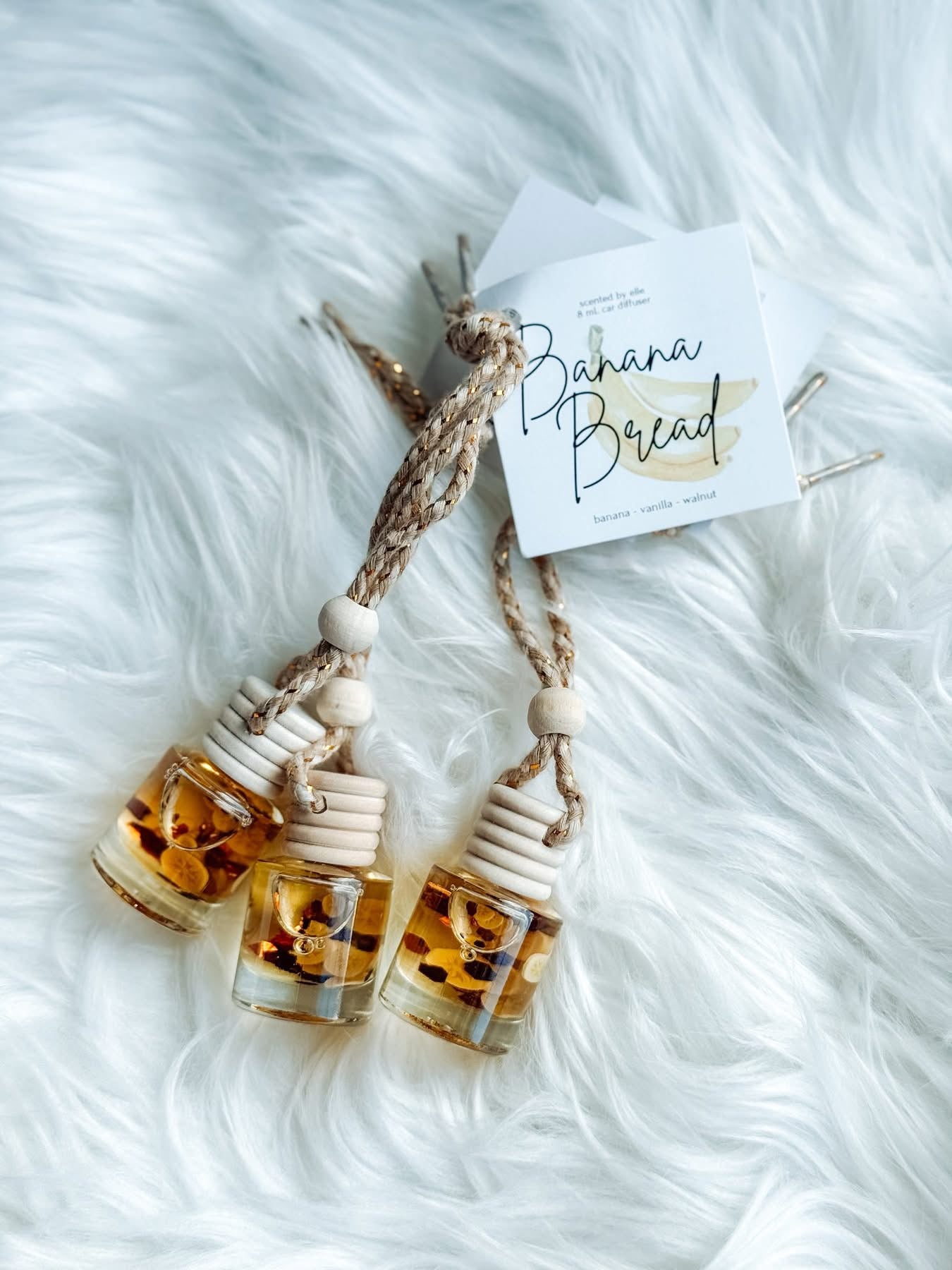 Two small glass bottles with a 'Banana Bread' label on a white fluffy surface