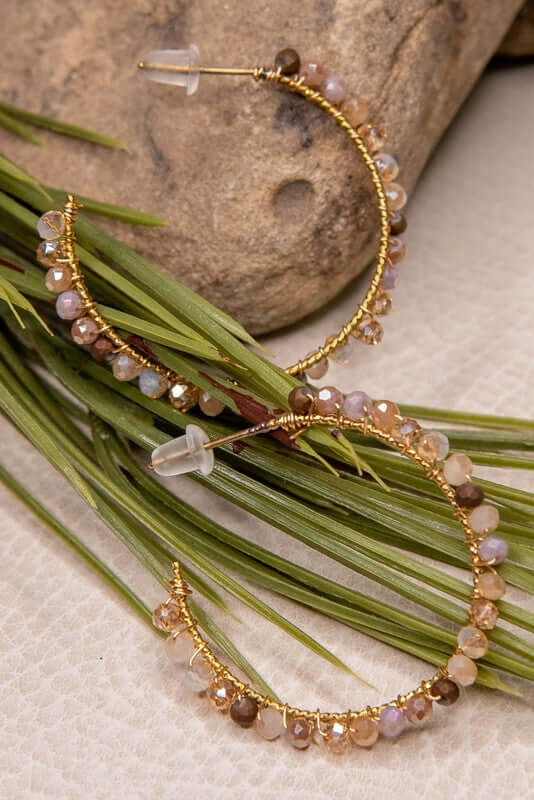Gold hoop earrings with gemstones on a stone and grass background
