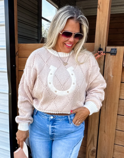 Tan cropped sweater featuring an all-over horseshoe pattern, styled on a model with high-waisted jeans and ankle boots. The cozy knit fabric and western-inspired design make it a perfect choice for layering or wearing solo for a trendy, casual look.