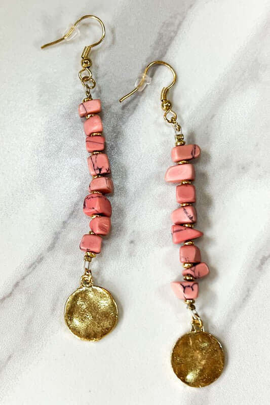 Pair of blush beaded earrings with gold disc charms on a marble background