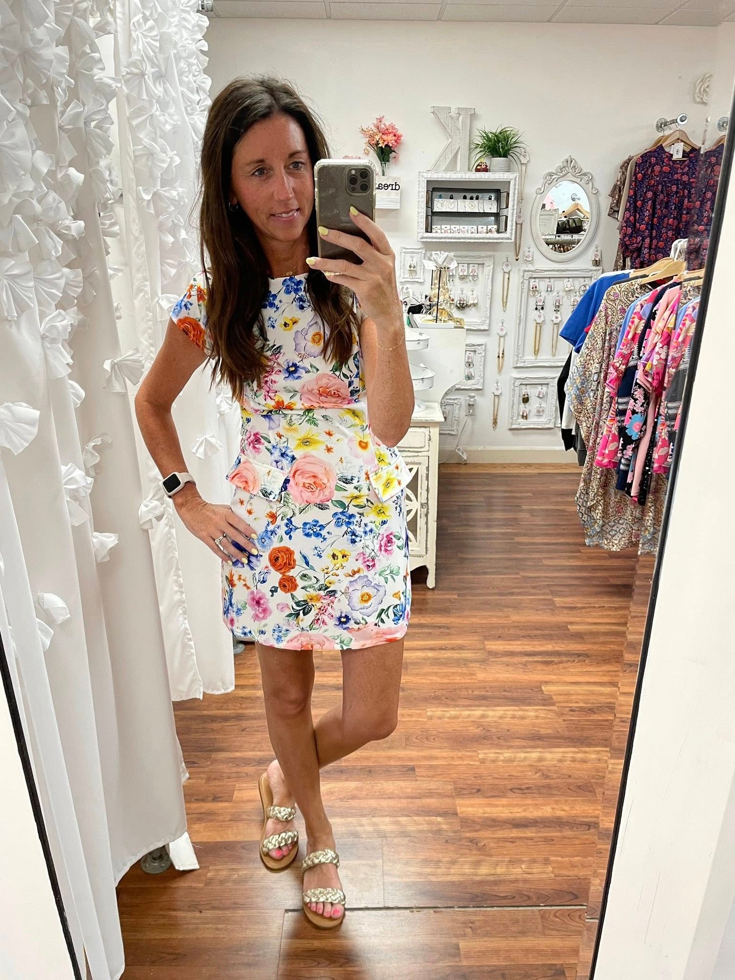 Woman taking a mirror selfie wearing a floral dress in a clothing store.