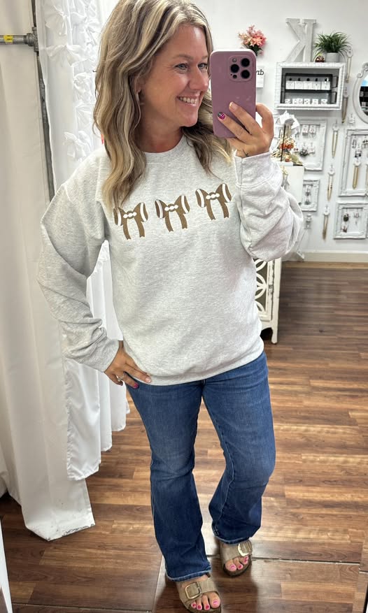 Woman taking a mirror selfie wearing a gray sweatshirt with gold letters and blue jeans.