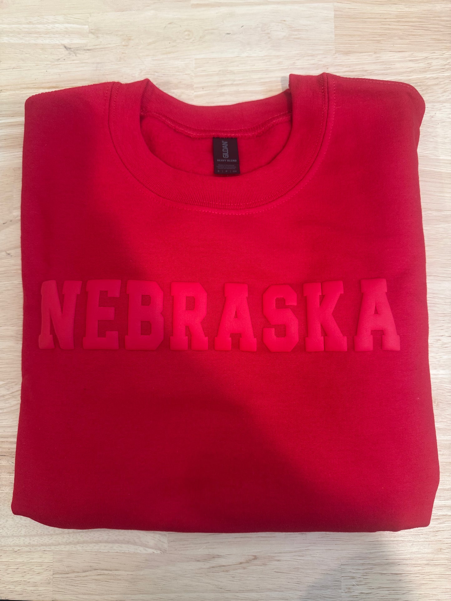 Folded red sweatshirt with 'NEBRASKA' text on a light wooden surface