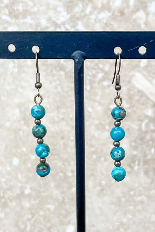 Pair of turquoise and silver beaded earrings on a stand with a light background
