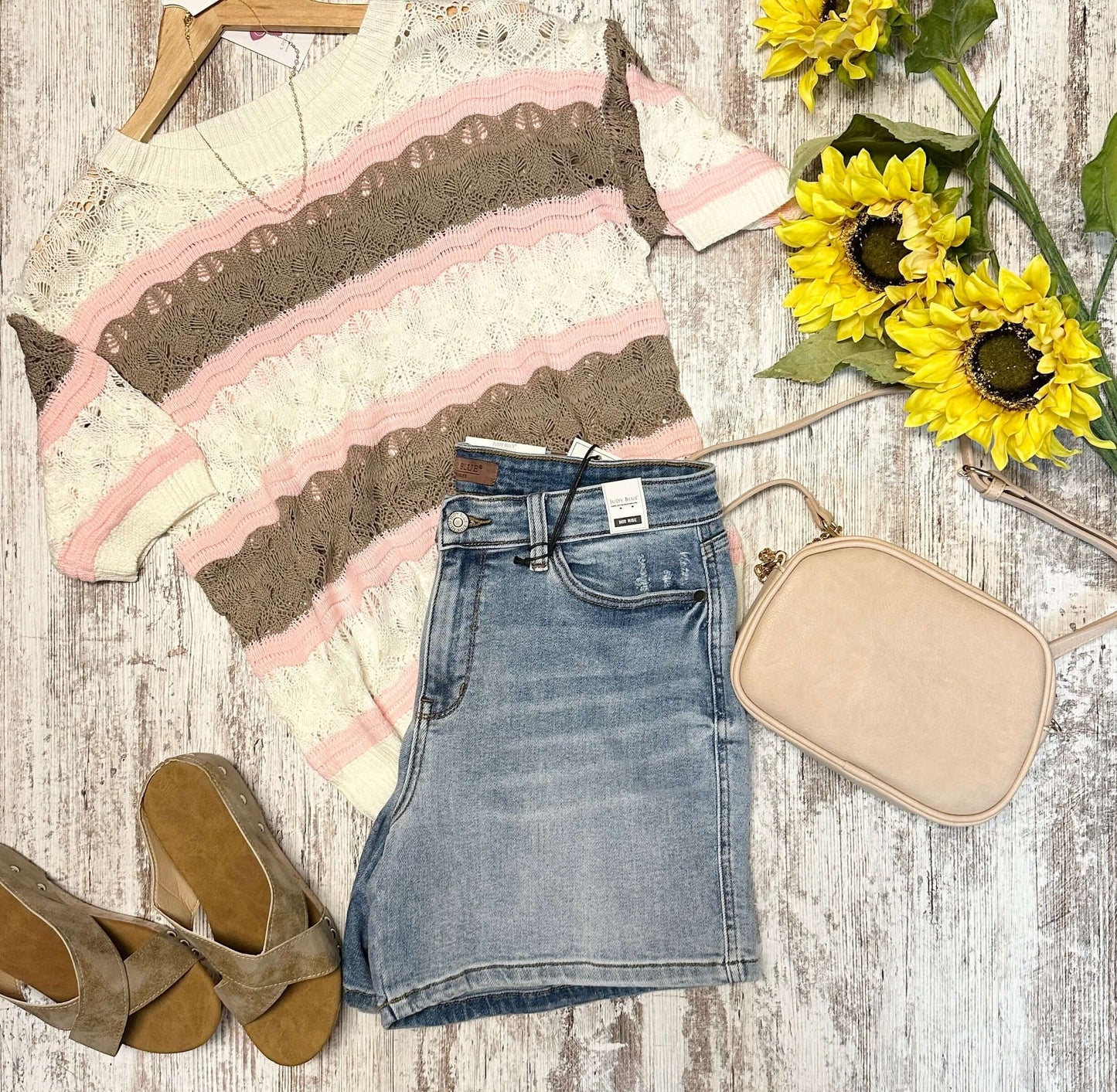 Denim skirt with lace top, beige purse, and sunflowers on a wooden surface