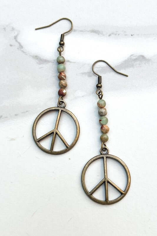 Peace sign earrings with beaded accents on a marble surface