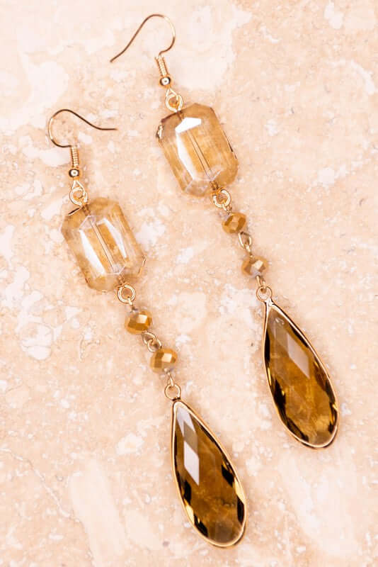 Pair of gold and brown teardrop earrings on a beige background