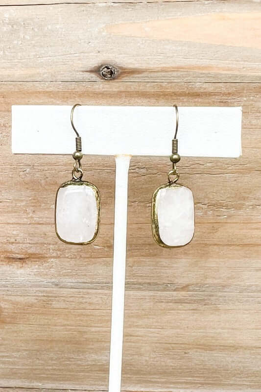 Pair of earrings with white stones and gold accents on a wooden surface