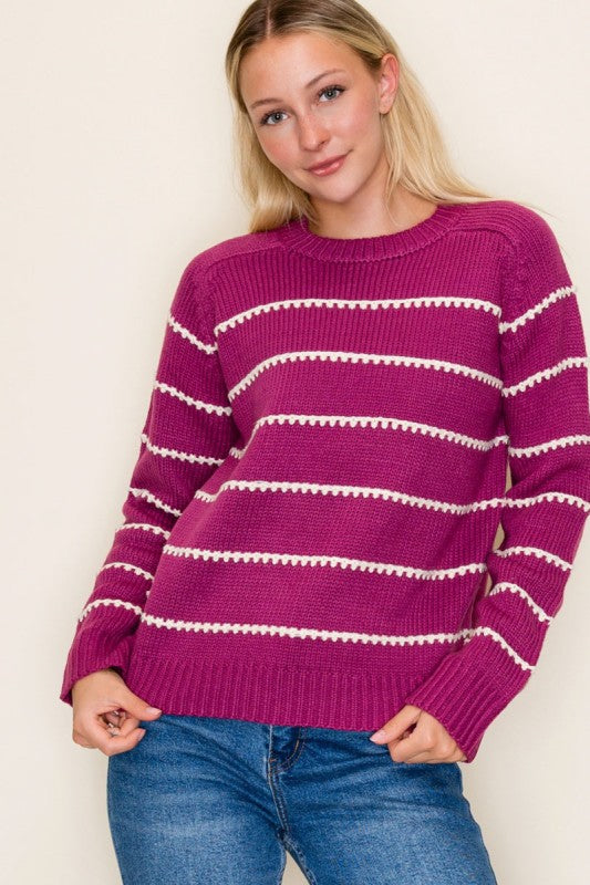 Woman wearing a magenta sweater with white stripes against a plain background