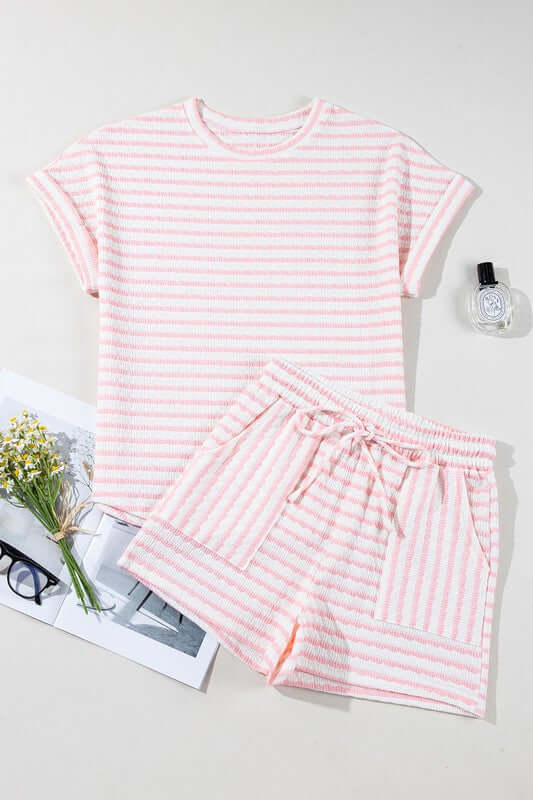 Pink and white striped pajama set on a light gray background with a magazine and flowers.