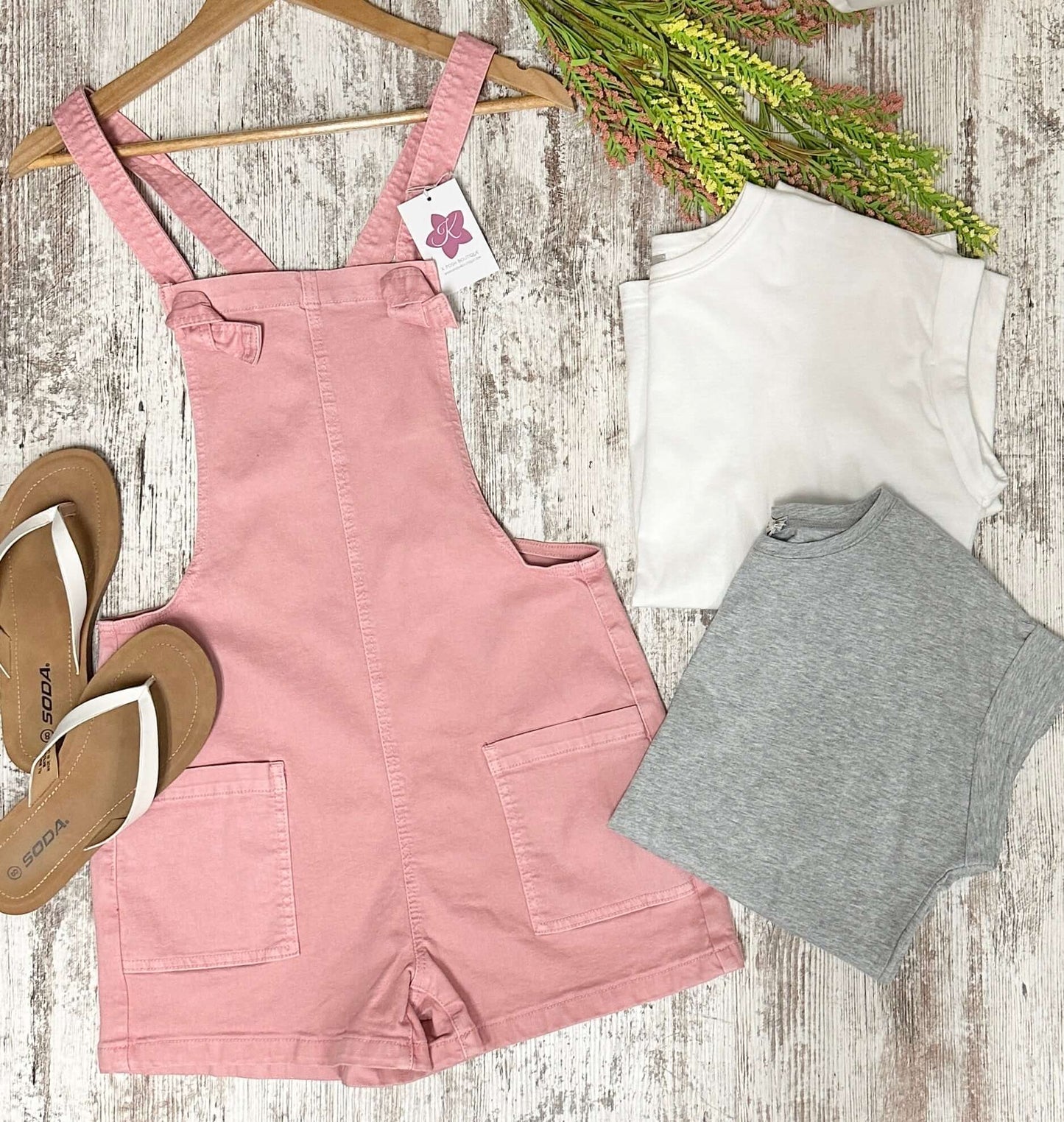 Pink overalls with a white t-shirt and gray shirt on a wooden surface.