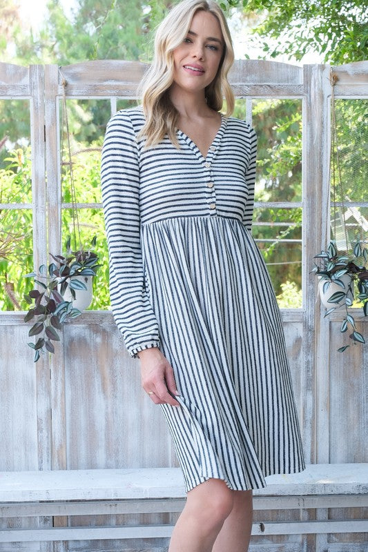 Woman wearing a striped dress sitting on a wooden bench with greenery in the background