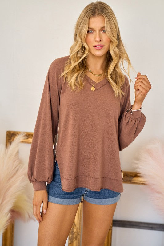 Woman wearing a brown long-sleeve top and denim shorts indoors.