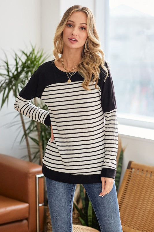 Woman wearing a black and white striped sweater with blue jeans indoors.