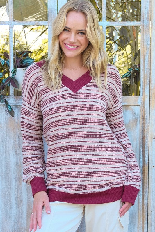 Woman wearing a maroon and beige striped sweater with a blurred outdoor background
