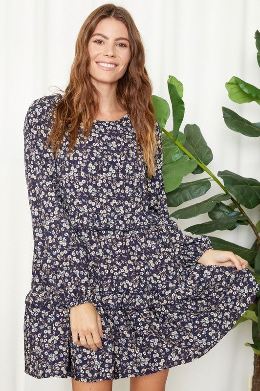 Woman wearing a navy floral dress standing next to a plant against a white background