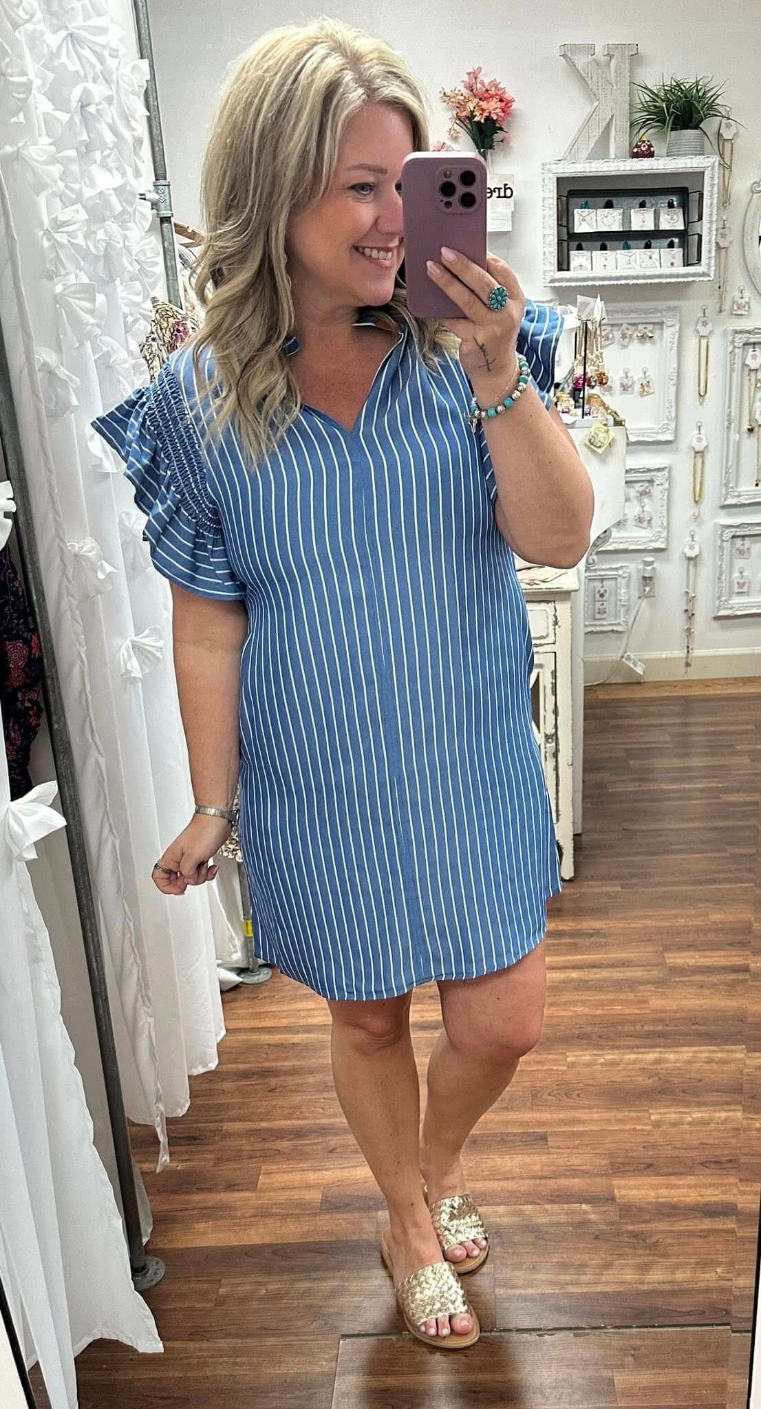 Woman taking a mirror selfie wearing a blue striped dress in a room with wooden flooring.