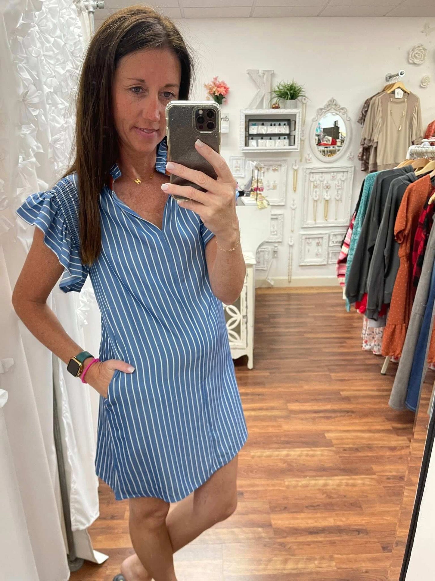 Woman taking a mirror selfie wearing a blue striped dress in a clothing store.