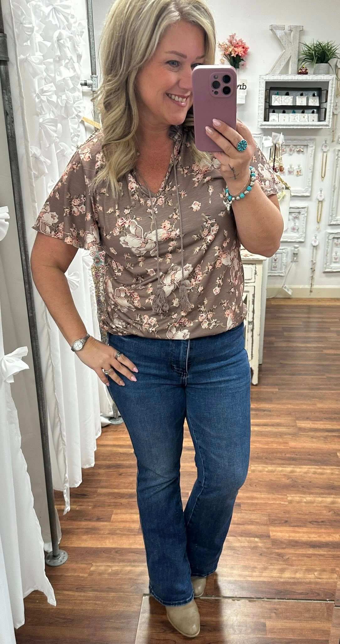 Woman taking a mirror selfie wearing a floral blouse and blue jeans in a store.