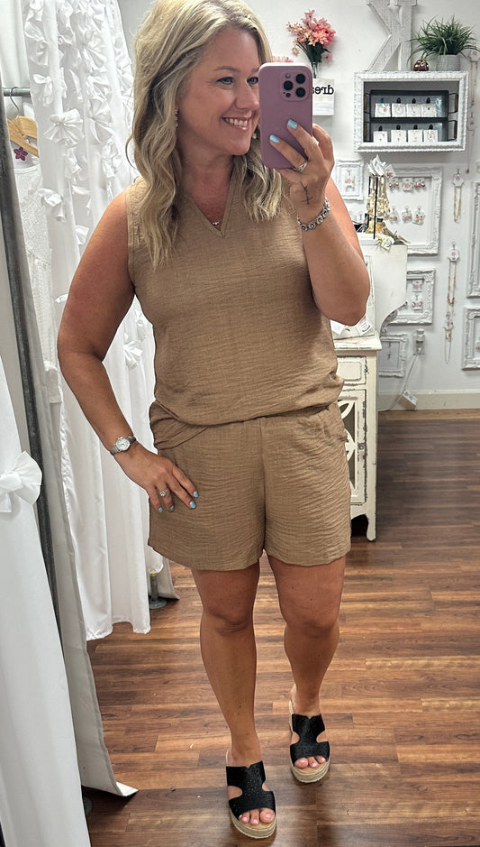 Woman taking a mirror selfie wearing a beige sleeveless top and shorts in a store.