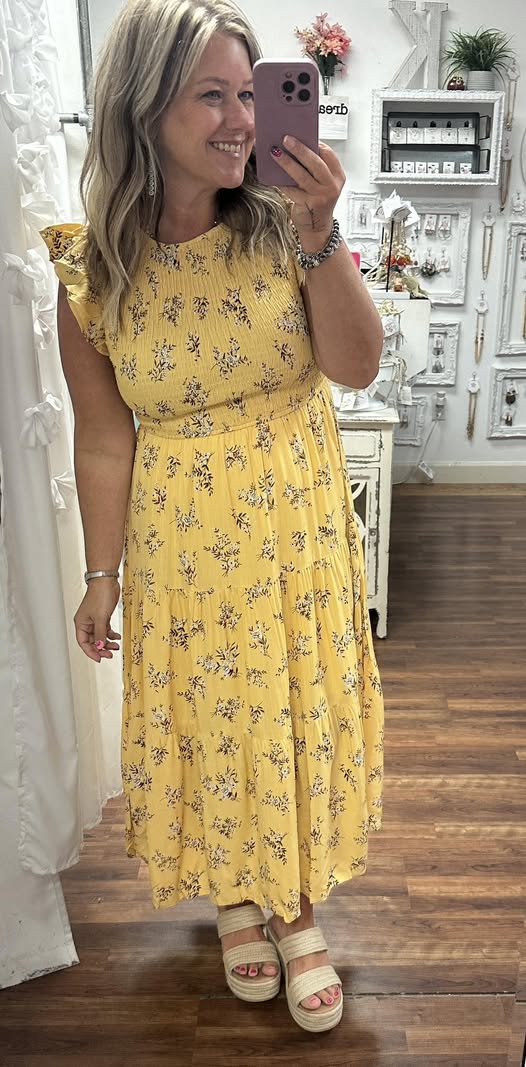 Woman taking a mirror selfie wearing a yellow floral dress in a store.
