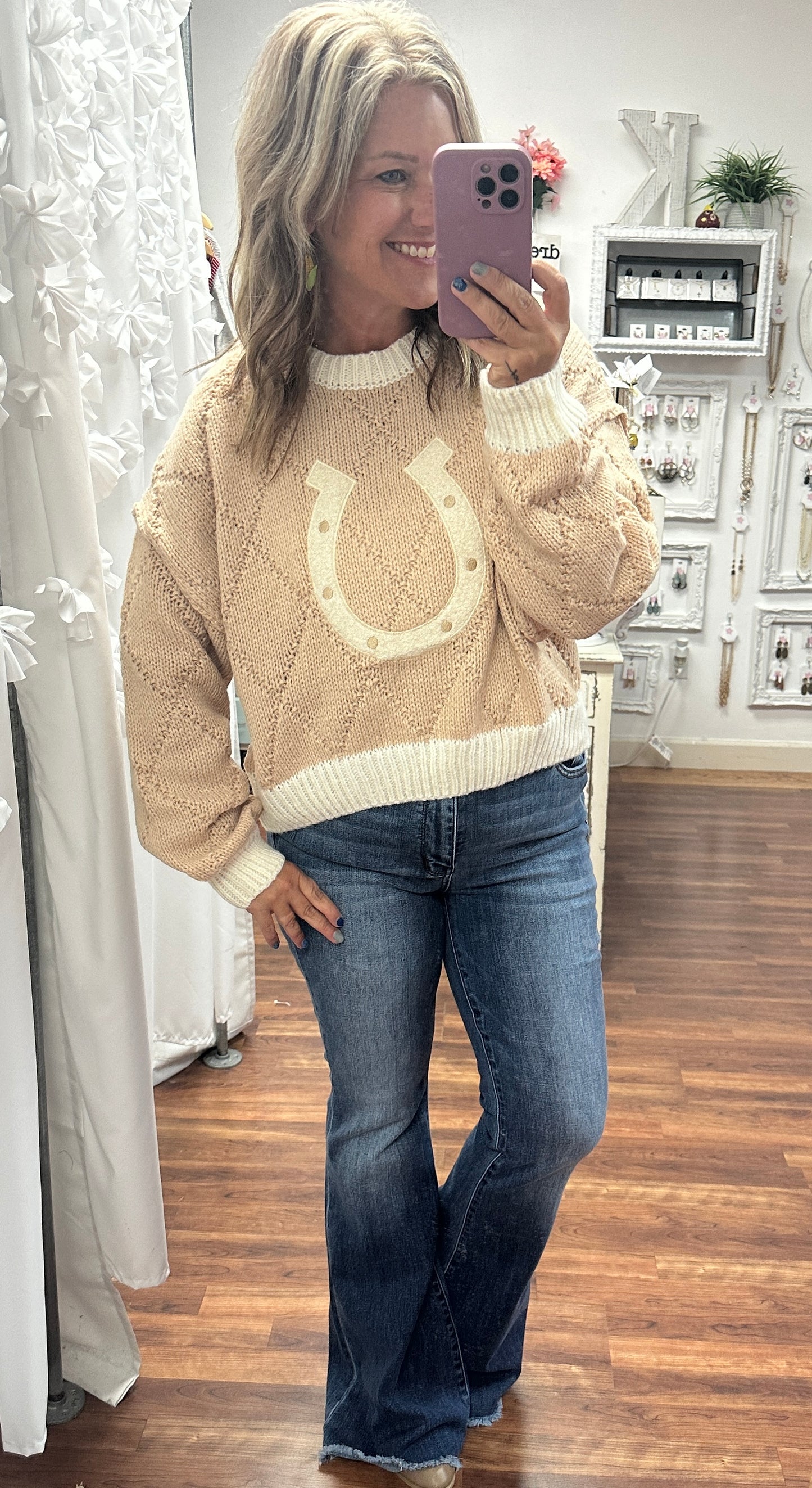 Tan cropped sweater featuring an all-over horseshoe pattern, styled on a model with high-waisted jeans and ankle boots. The cozy knit fabric and western-inspired design make it a perfect choice for layering or wearing solo for a trendy, casual look.