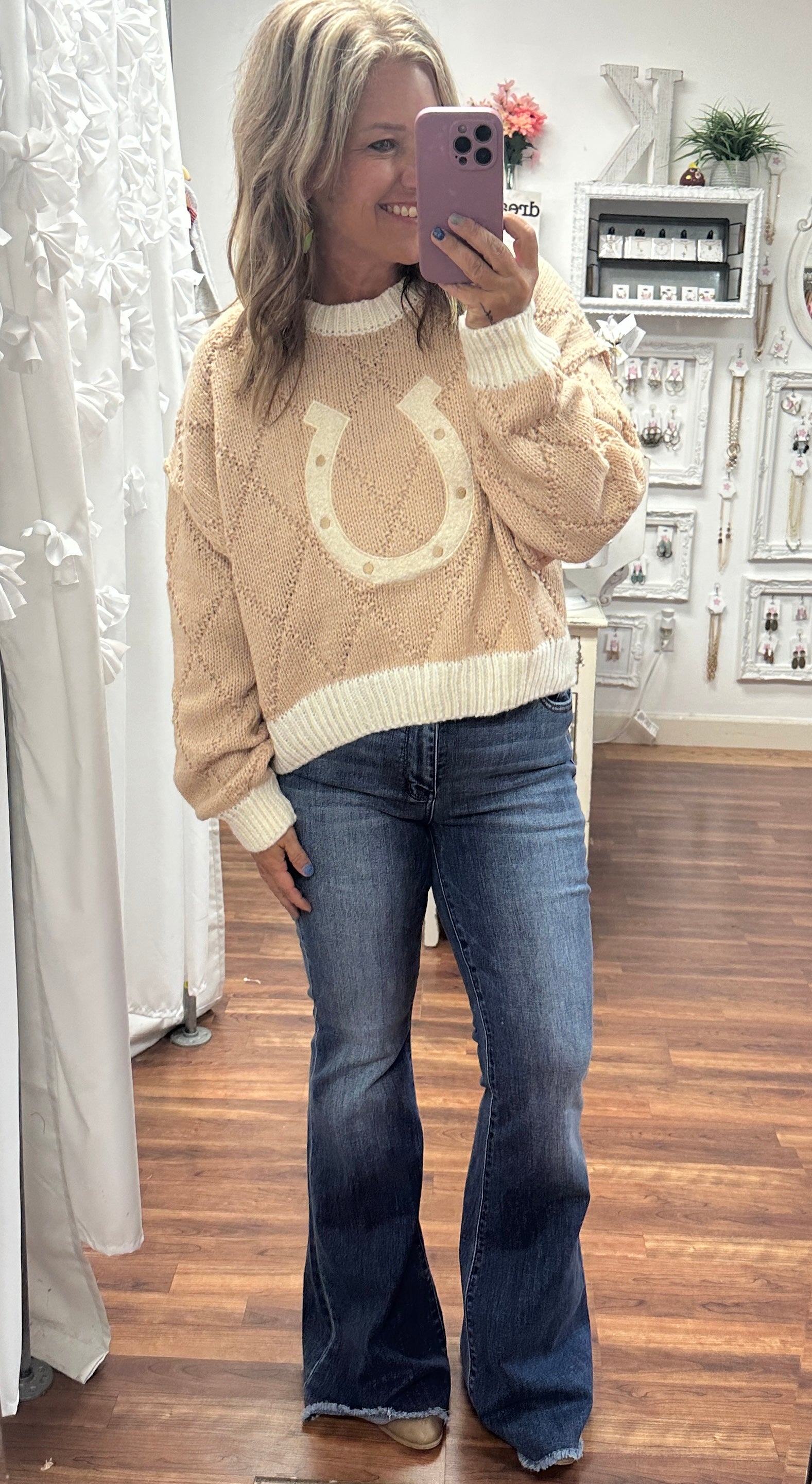 Tan cropped sweater featuring an all-over horseshoe pattern, styled on a model with high-waisted jeans and ankle boots. The cozy knit fabric and western-inspired design make it a perfect choice for layering or wearing solo for a trendy, casual look.