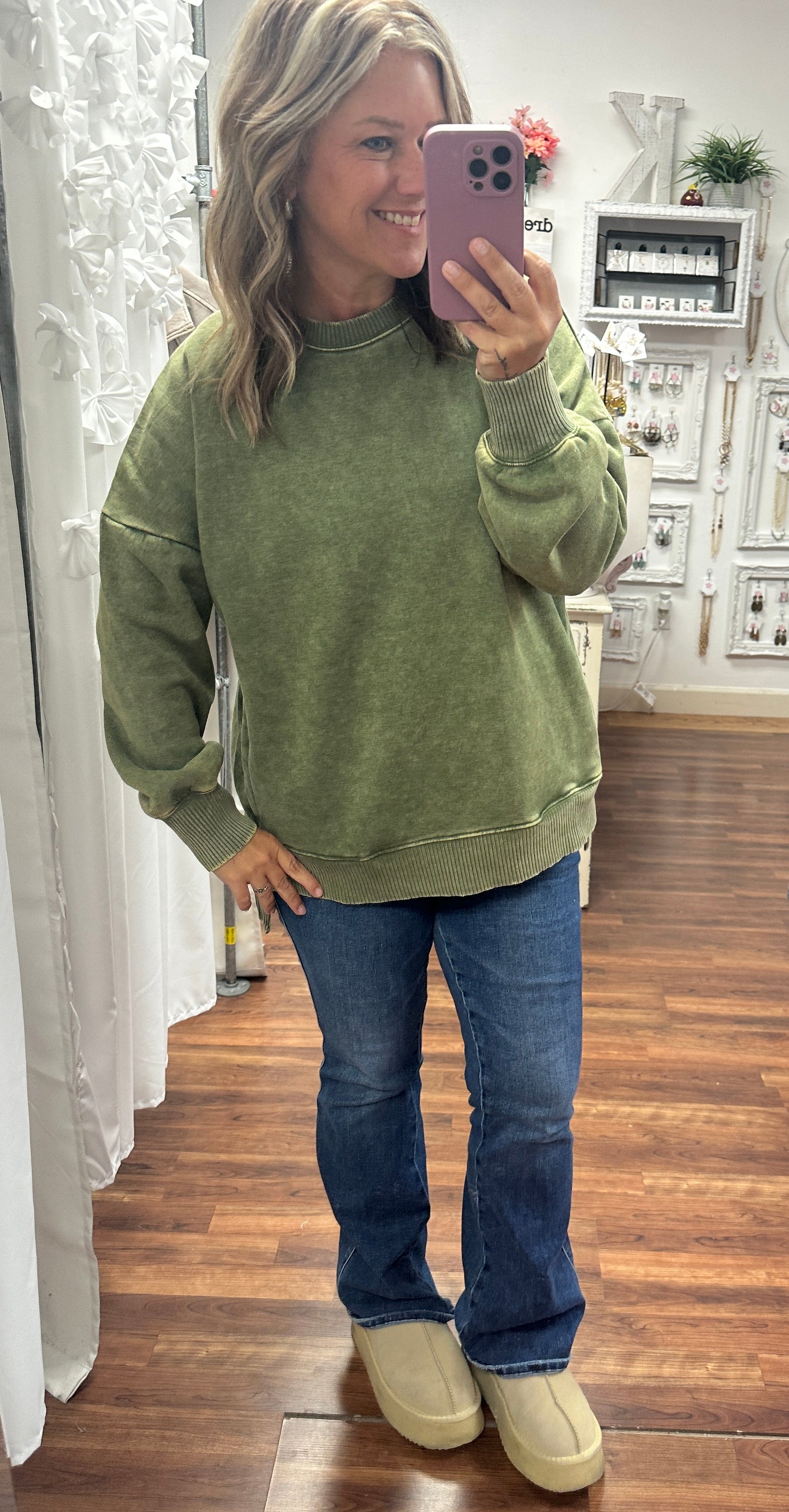 Person wearing a green sweatshirt and blue jeans taking a mirror selfie.