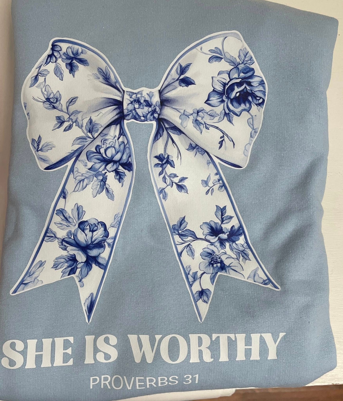 Floral bow design on a light blue background with 'SHE IS WORTHY' text.