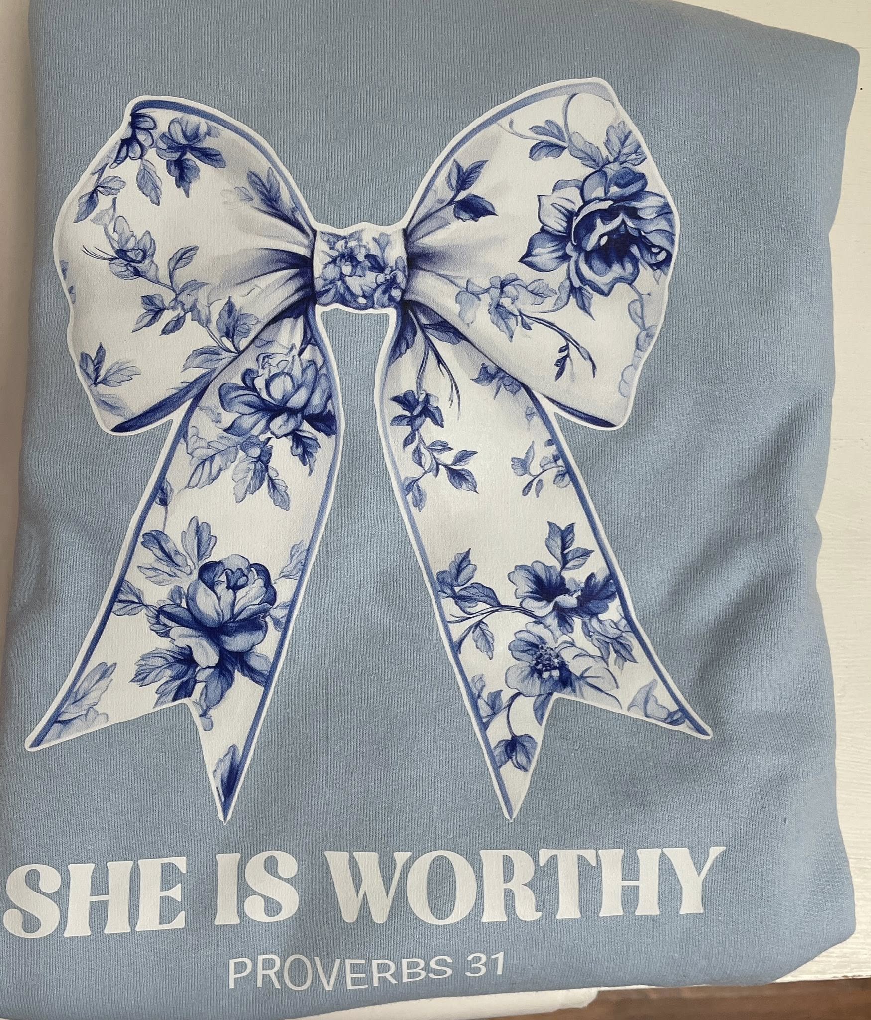 Floral bow design on a light blue background with 'SHE IS WORTHY' text.