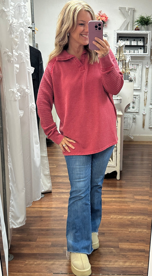 Woman taking a mirror selfie wearing a pink sweater and blue jeans in a store.