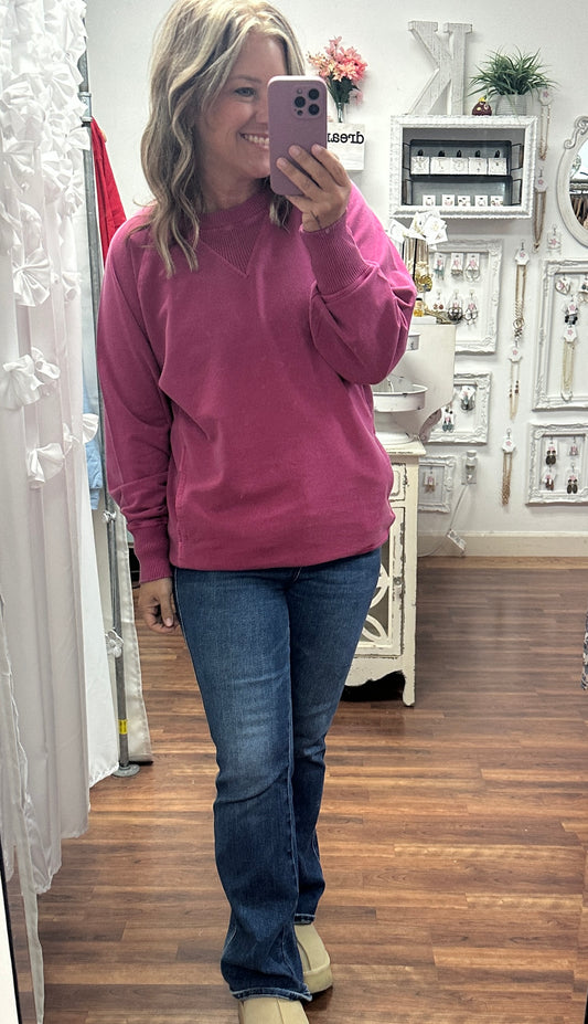 Person taking a mirror selfie wearing a pink sweatshirt and blue jeans in a store.