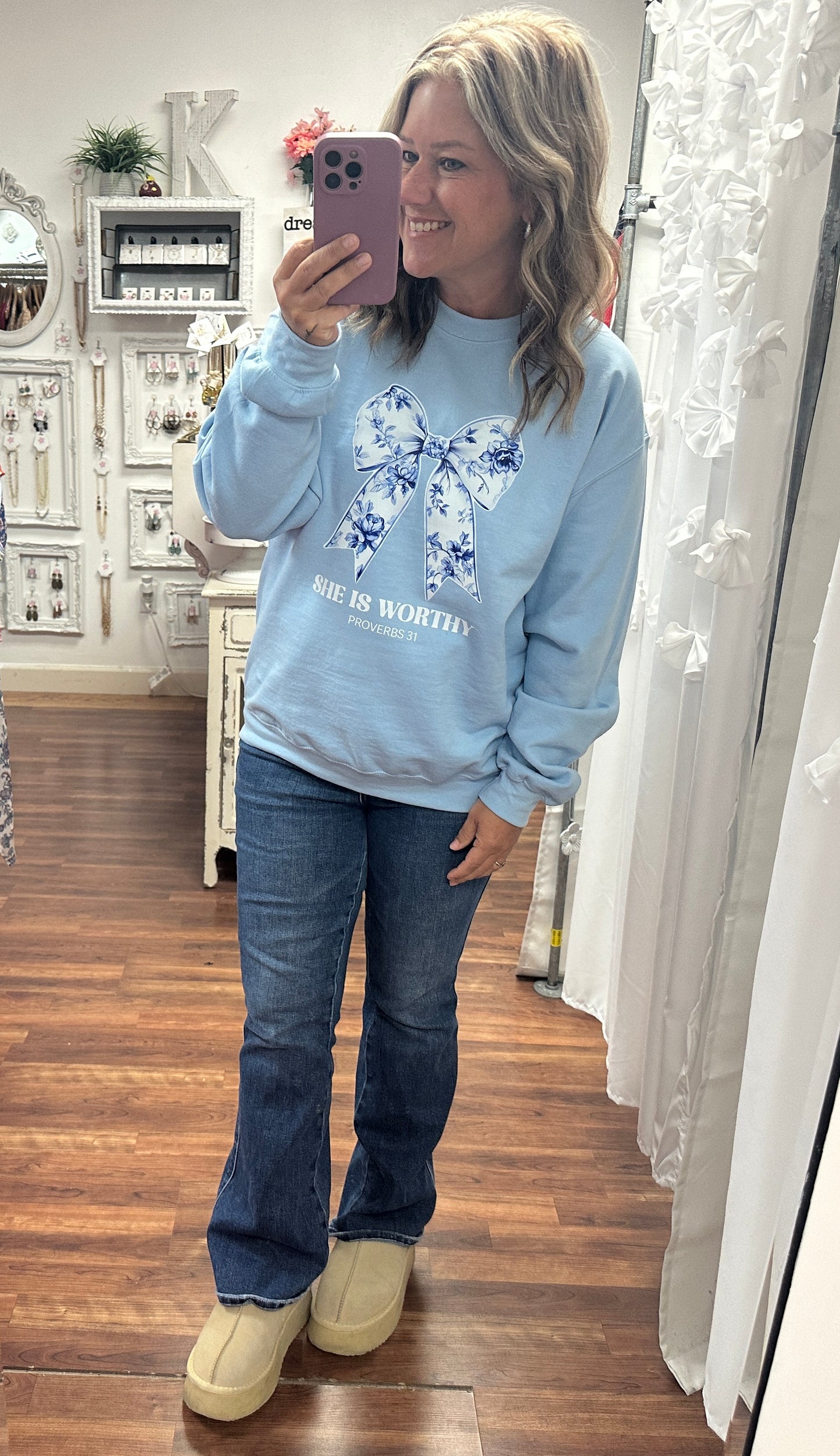 Person wearing a light blue sweatshirt with a floral design and text, standing in a room.