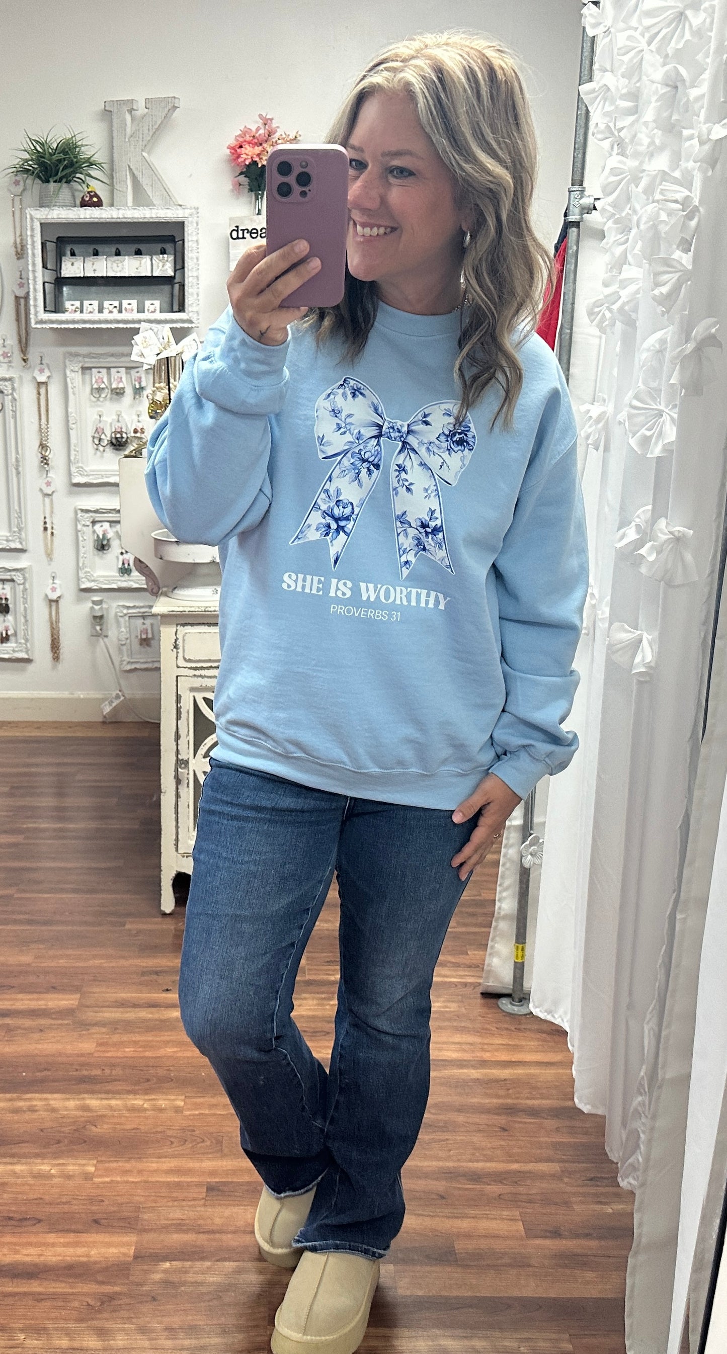 Person wearing a light blue sweatshirt with a floral design and text, standing in a room.