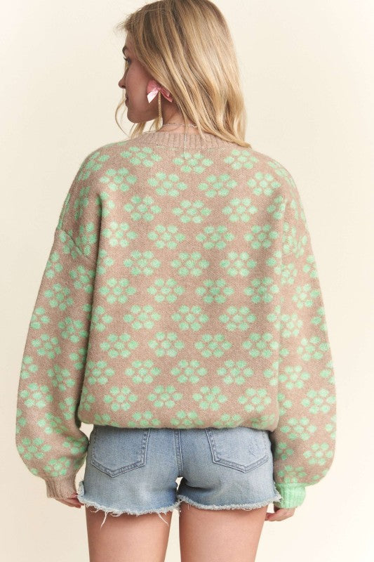 Person wearing a pink sweater with green floral pattern and denim shorts on a beige background