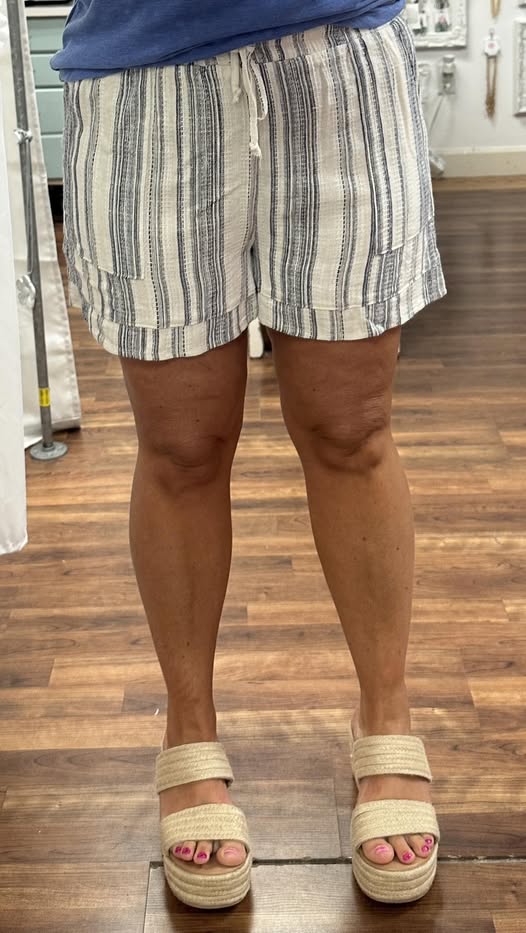 Person wearing striped shorts and platform sandals on a wooden floor.