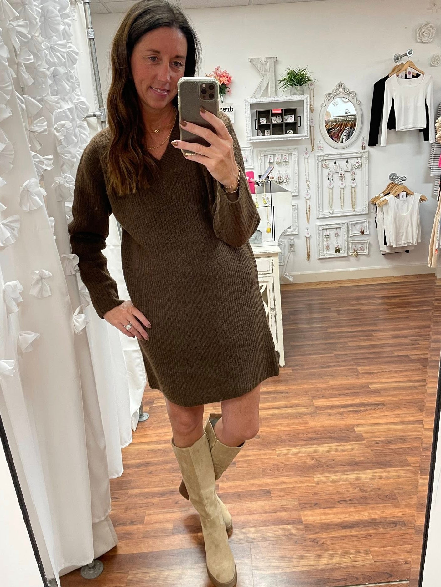 Woman taking a mirror selfie wearing a brown dress and beige boots in a store.
