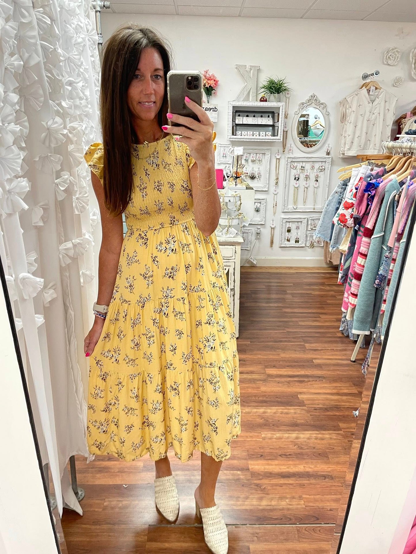 Woman taking a mirror selfie wearing a yellow floral dress in a clothing store.