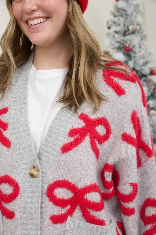 Person wearing a gray cardigan with red bows in front of a Christmas tree.