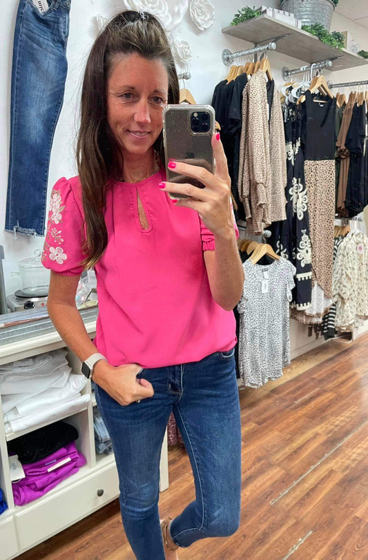 Woman taking a mirror selfie wearing a pink top and blue jeans in a clothing store.