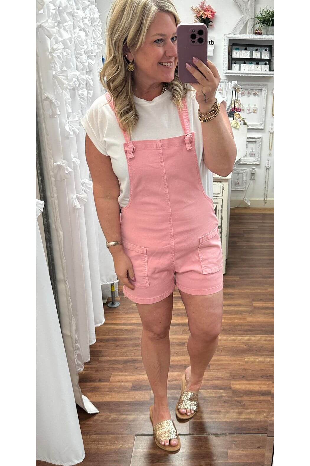 Woman wearing a pink overall dress taking a mirror selfie.