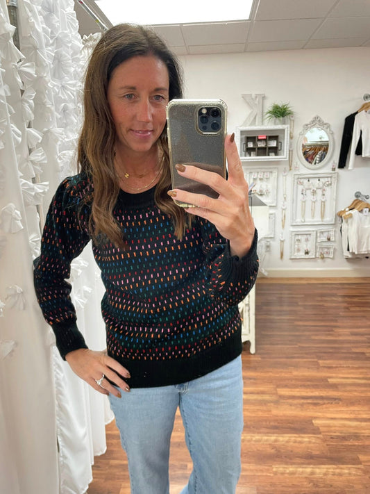 Woman taking a mirror selfie wearing a patterned sweater in a store setting.