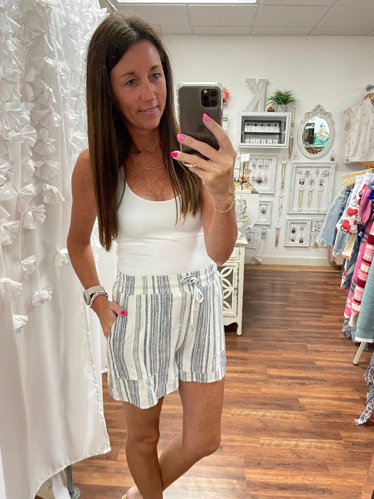 Woman taking a mirror selfie wearing a white top and striped shorts in a store.